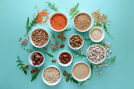 Set of bowls with organic quinoa, lentil, chickpea, wheat, walnut, almond, hazelnut and sesame. Cereals and legumes assortment on blue paper background. Top view. Copy space. Flat layの写真素材