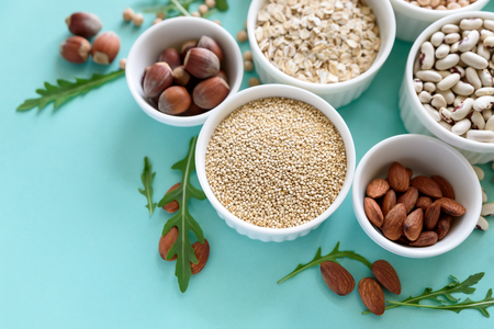 Set of bowls with organic quinoa, lentil, chickpea, wheat, walnut, almond, hazelnut and sesame. Cereals and legumes assortment on blue paper background. Top view. Copy space. Flat layの写真素材