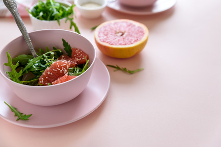 Fresh citrus salad with arugula, grapefruit and sesame seeds on pink background. Selective  focus. Raw vegetarian spring detox food.の写真素材