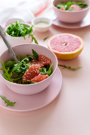Fresh citrus salad with arugula, grapefruit and sesame seeds on pink background. Selective  focus. Raw vegetarian spring detox food.の写真素材