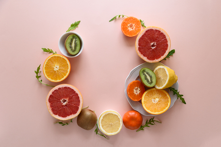 Tropical fruits frame from orange, lemon, tangerine and kiwi on pink paper background. Healthy food concept. flat lay. Top viewの写真素材
