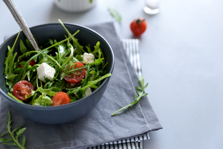 Bowl of arugula salad with tomatoes and feta sheese on gray wooden background. Vegetarian food conceptの写真素材