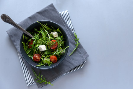 Bowl of arugula salad with tomatoes and feta sheese on gray wooden background. Vegetarian food conceptの写真素材