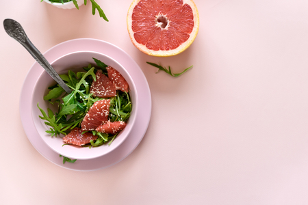 Fresh citrus salad with arugula, grapefruit and sesame seeds on pink background. Selective  focus. Raw vegetarian spring detox food.の写真素材
