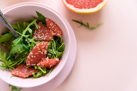 Fresh citrus salad with arugula, grapefruit and sesame seeds on pink background. Selective  focus. Raw vegetarian spring detox food.の写真素材