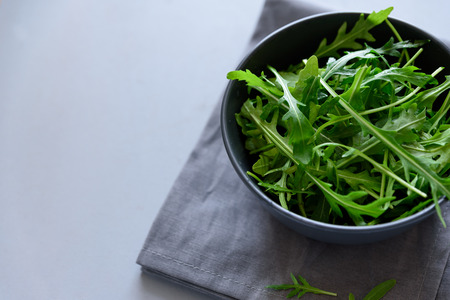 Fresh green arugula in bowl on gray wooden background. Healthy food or vegetarian concept. Top view. Copy spaceの写真素材