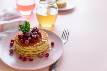Stack of pancakes with frozen raspberry, red currant and honey on pink background. Selective focusの写真素材