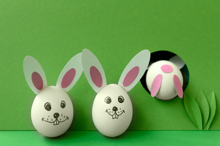Easter bunny made from eggs and paper ears jump in hole on green pastel background. Creative idea....