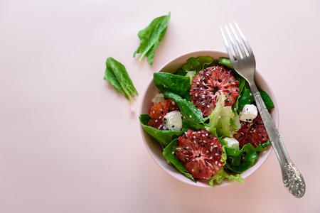 Spring fresh salad with blood orange, lettuce, spinach and sesame seeds on pink background. Top view. Selective focusの写真素材