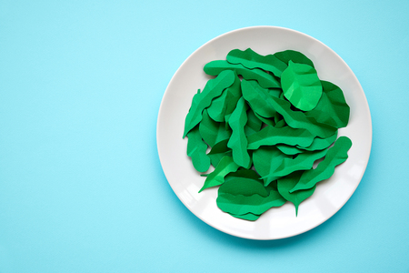 Plate with greens made from paper: spinach and arugula on blue background. Minimal, creative, vegan, healthy or food art concept. Copy space. Top viewの写真素材