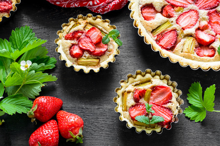 Homemade tarts with strawberry and rhubarb on black wooden background. Top view. Rustic styleの写真素材