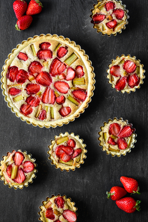 Homemade tarts with strawberry and rhubarb on black wooden background. Top view. Rustic styleの写真素材