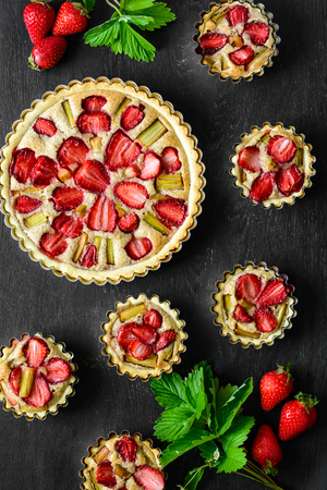 Homemade tarts with strawberry and rhubarb on black wooden background. Top view. Rustic styleの写真素材