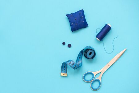 Sewing accessories with threads, scissors, pins, fabric, buttons and sewing tape on blue background. Top view. Flat lay.の写真素材