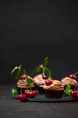 Chocolate cupcakes with ripe red cherries on dark wooden background. Selective focus. Unhealthy foodの写真素材