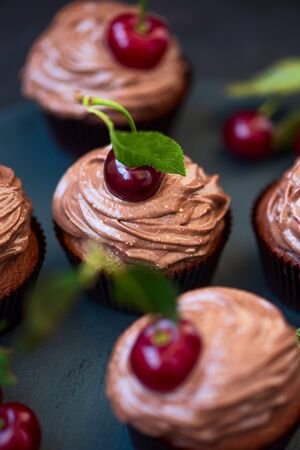 Chocolate cupcakes with ripe red cherries on dark wooden background. Selective focus. Unhealthy foodの写真素材