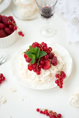 Pavlova fruit cake with strawberry, raspberry, red currant and mint leaves on white background. Selective focus. Healthy food conceptの写真素材