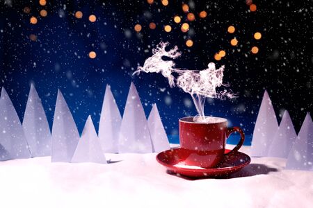 Steam in reindeer and Santa Claus into sled shape flying over red mug of coffee or tea in snowy landscape. Christmas or New Year celebration concept. Copy spaceの写真素材