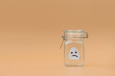 Paper craft. White ghost in glass jar on orange background. Halloween celebration concept. Copy spaceの写真素材