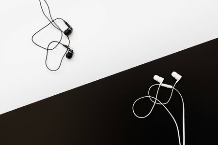 White earphones for smartphone on black and black earphones on white background. Top view on personal accessories.の写真素材