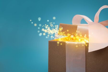 Open gift box wrapped ribbon with magical light on blue background. Christmas and New Year holidays conceptの写真素材
