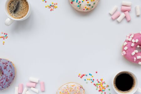 Frame from cups of espresso coffee and sweet donuts decorated marshmallow and colorful sprinkles on white background. Flat lay. Top view. Unhealthy foodの写真素材