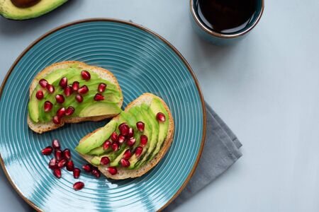 Avocado sandwich on bread made with fresh sliced avocados and pomegranate seeds on gray wooden background. Top view. Healthy eating concept. Copy spaceの写真素材