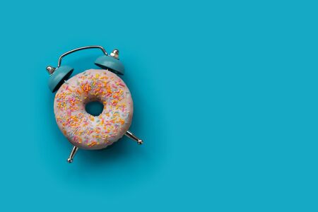 Pink alarm clock donut on blue background. Breakfast time or minimal concept. Copy space. Top viewの写真素材