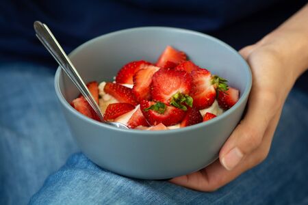 Woman's hands holding smoothie or granola bowl topped with fresh strawberry. Healthy breakfast conceptの写真素材