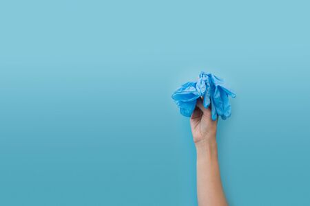 Hand holding medical gloves on blue background.  Flu, illness, pandemic concept