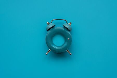 Vacation time. Blue alarm clock as swimming ring form on blue background. Top view. Copy spaceの写真素材