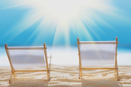 Deck chairs on sandy beach with blurry blue ocean and sun beams on sky. Social distancing or COVID-19 protection at summer holidays. Summer background. Soft focusの写真素材