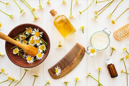 Chamomile flowers and cosmetic bottles of essential oil and extract on white wooden background. Flat lay. Top view. Copy spaceの写真素材