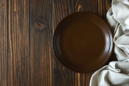 Rustic kitchen table with empty brown plate and towel on brown wooden background. Top view. Copy space. Flat layの写真素材