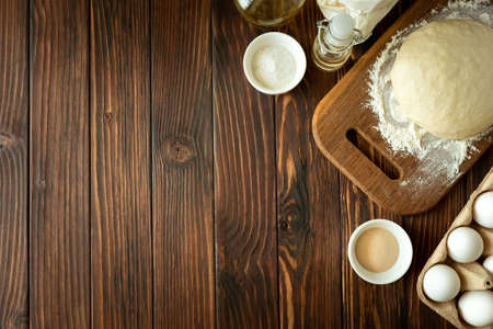 Baking in rural kitchen. Dough and recipe ingredients on vintage brown wooden table. Top view....