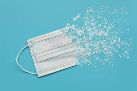Protective mask with dispersion effect on blue background. Covid-19, quarantine end concept. Top...