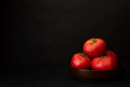 Fresh ripe tomatoes in bowl on dark background. Copy space