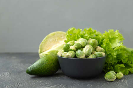 Green vegetables. Bowl with raw brussels sprouts, avocado, cabbage and lettuce on concrete...