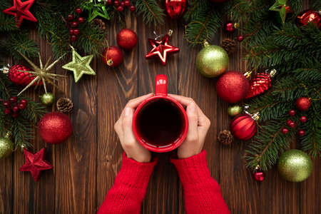 Woman holding hot Christmas tea against decorations on wooden table. Top view. New Year or Christmas...