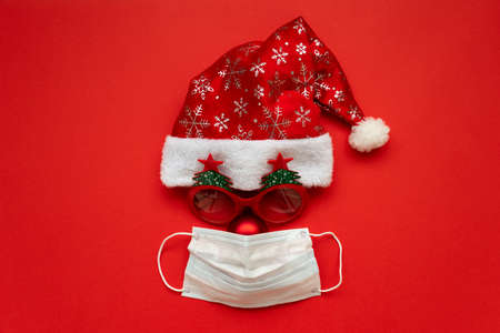 Santa Claus hat, glasses and nose with face mask on red background. Flat lay. Christmas or New Year...