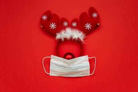 Christmas reindeer made from face mask and decorations on red background. Flat lay. Christmas or New Year celebration conceptの写真素材