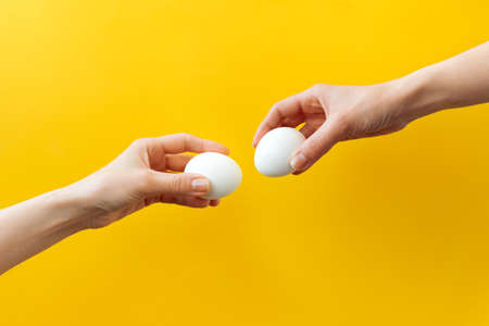 Woman hands holding Easter eggs for knocking on yellow background. Easter celebration or creative...