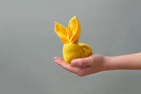 Boy holding figure of Easter bunny made of napkin on gray background. DIY. Easter celebration concept. Soft focusの写真素材
