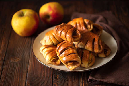 Homemade rolls buns with apples and cinnamon on brown wooden background. Soft focus
