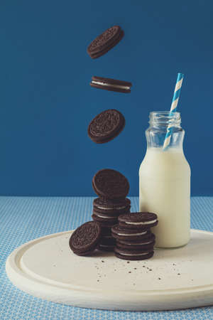 Flying chocolate cookies with milk on blue paper background. Breakfast food