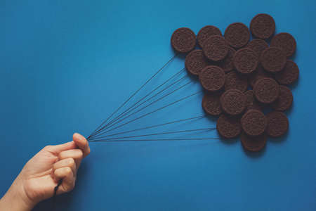 Hand holding balloons made of chocolate cookies on blue paper background. Creative concept. Flat layの写真素材