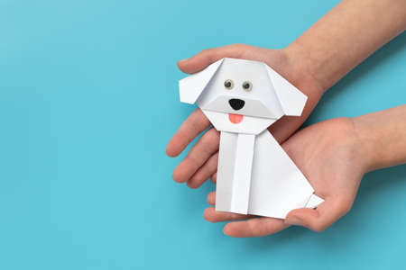 Child hands holding white paper dog on blue background.