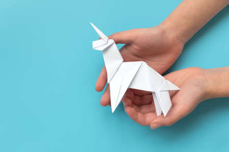 Child hands holding white paper unicorn on blue backgroundの写真素材