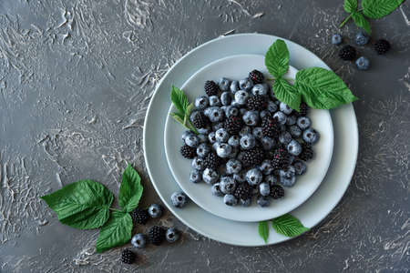 Fresh blueberries and blackberries decorated green leaves on gray concrete background. Top viewの写真素材