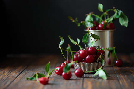 Close-up ripe red cherries against bowl with berries on brown wooden table. Soft focusの写真素材
